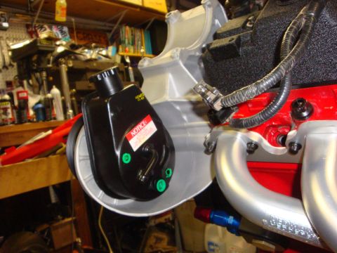 1989 Ford Bronco - A power steering pump with a 'NOTICE' sticker is mounted on a red engine block in a garage setting.
