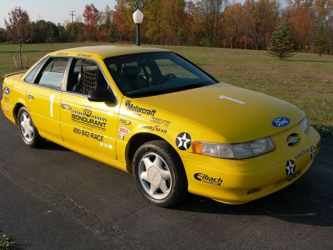 1993 Ford Taurus - A yellow Ford Taurus, likely a 1993 model, is parked on asphalt with a grassy background and trees.