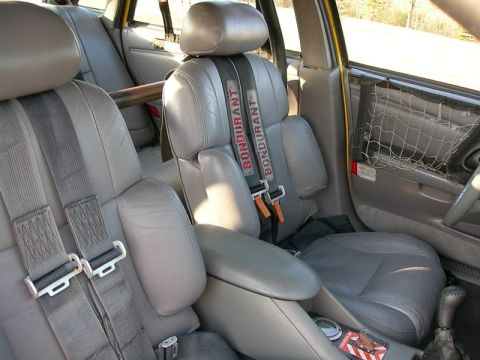 1993 Ford Taurus - The interior of a car shows racing seats and a roll cage, with visible 'Bondurant' branding on the harnesses.