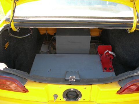 1993 Ford Taurus - The trunk of a yellow car contains a custom subwoofer box and a fire extinguisher, suggesting modifications.