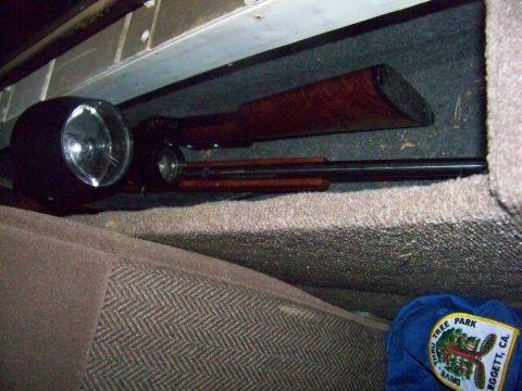1989 Ford Bronco - A rifle and flashlight are visible under the seat of a vehicle, with a hat from Tree Park Drive in Eggert, CA nearby.
