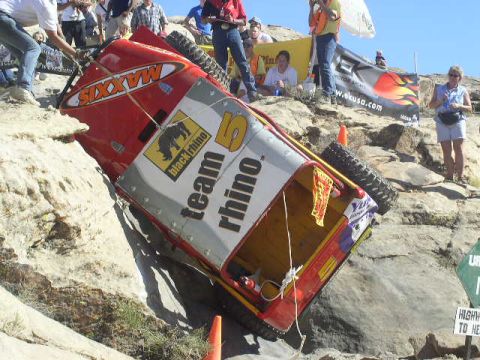 1979 Ford Bronco - A red off-road vehicle navigates a rocky course, displaying 'Team Rhino' branding and Maxxis tires.