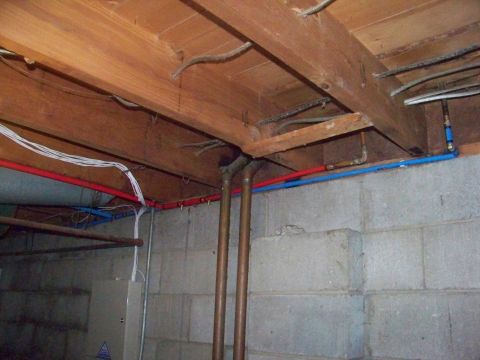 1989 Ford Bronco - A view of plumbing and electrical work in a basement, showing pipes and wires running along a concrete block wall.