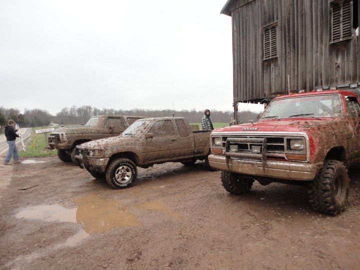 Red Dodge pickup truck in front of muddy field and barn
