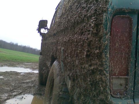 1979 Ford Bronco - This heavily mud-caked SUV is seen from the rear quarter panel, with a muddy field and trees in the background.