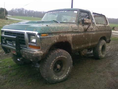 1979 Ford Bronco - This heavily muddied 1978 Ford Bronco is shown from a three-quarter front angle, highlighting its off-road tires and weathered condition.