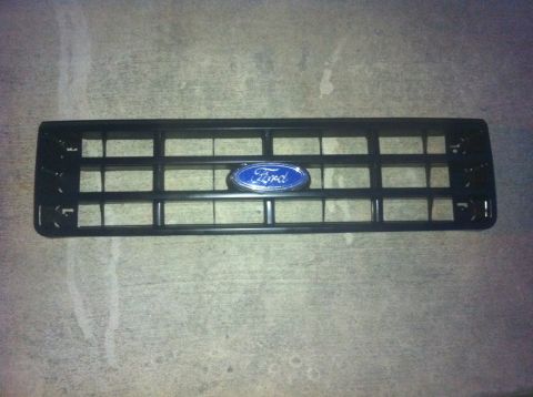 1990 Ford Bronco - A black Ford grille with the blue oval Ford emblem is shown against a concrete background.