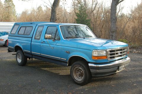 1992 Ford F-150 - A blue 1992 Ford F-150 pickup truck with a camper shell is parked outdoors.