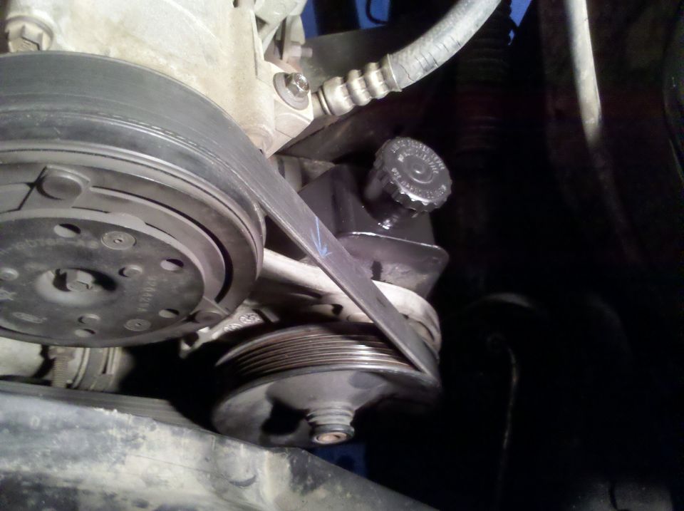 Close-up of power steering pump pulley, reservoir cap, serpentine belt and A/C compressor pulley on an engine