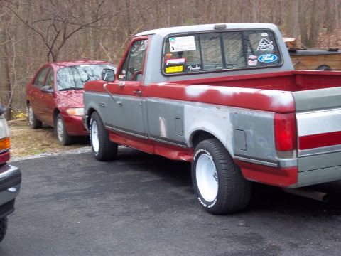 1989 Ford F-150 - A red and gray Ford F-150 pickup truck is parked next to a red sedan. The truck has some bodywork in progress.