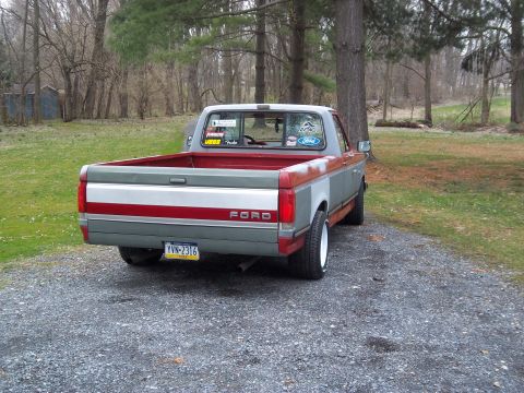 1989 Ford F-150 - This Ford pickup truck has a two-tone paint scheme with a red stripe and a 'FORD' badge on the tailgate.