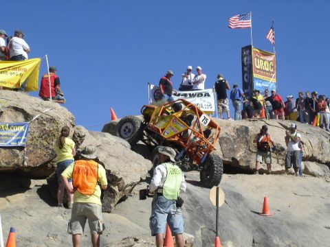 1979 Ford Bronco - A custom off-road buggy navigates a steep rocky course during a competition, with American flags and banners visible in the background.