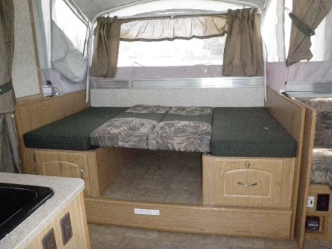 2007 Dodge 2500 - The interior of a pop-up camper shows a bed area with storage cabinets and curtains.