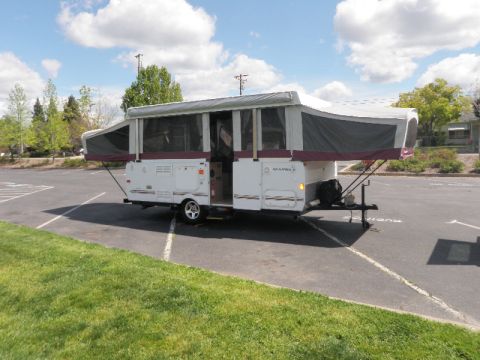 2007 Dodge 2500 - A white pop-up camper trailer is parked in an asphalt lot under a partly cloudy sky.
