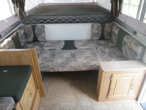2007 Dodge 2500 - Interior of a pop-up camper with a dinette that converts to a bed and an overhead sleeping area.