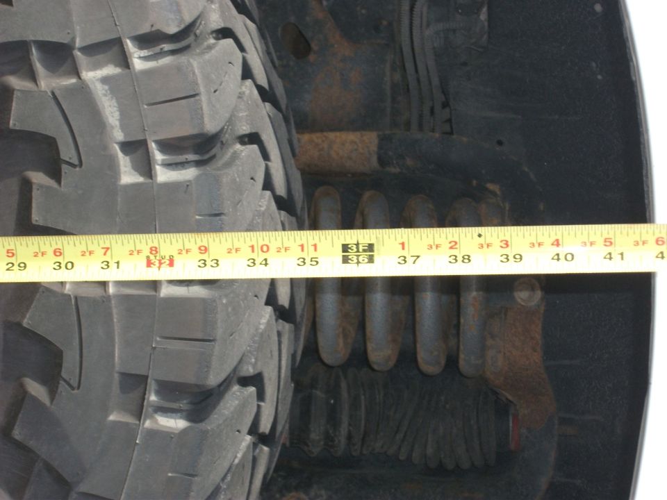 Close-up of a large tire with a yellow measuring tape across it, showing suspension components behind