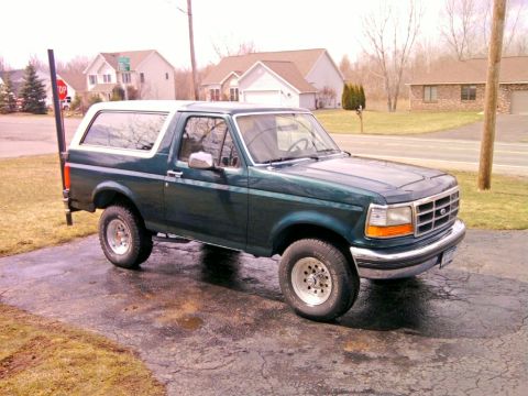 1993 Ford Bronco - This green Ford Bronco is parked on a wet driveway with houses in the background.