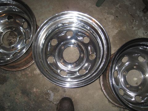 1979 Ford Bronco - Several shiny chrome wheels are laid out on a concrete floor.