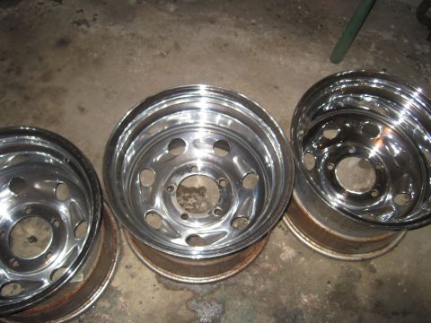 1979 Ford Bronco - Three chrome wheels are displayed on a concrete floor, with visible rust on the inner barrels.
