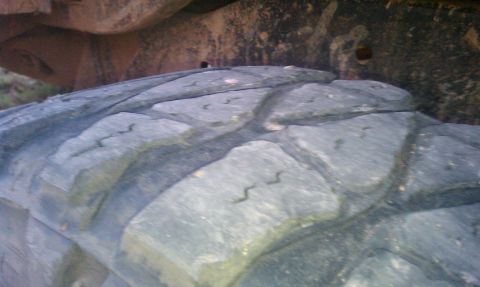 1979 Ford Bronco - A close-up view shows the tread pattern of a large vehicle tire, with the frame and suspension visible above.