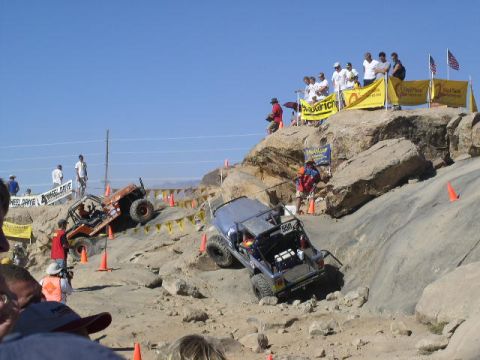 1979 Ford Bronco - Competitors tackle a challenging rocky course with spectators cheering from the hillside.