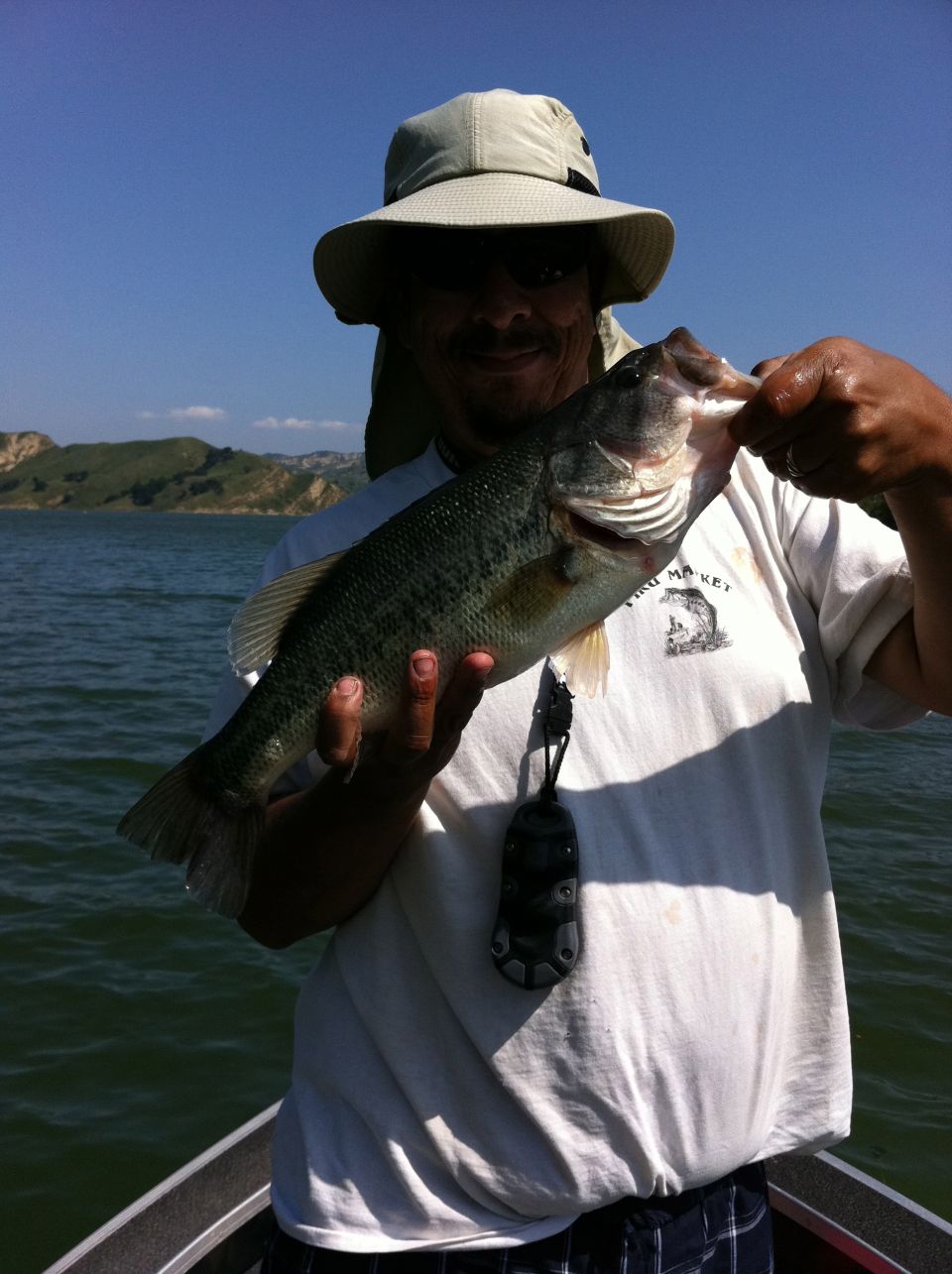 Man in a hat and t-shirt holds a large bass while standing in a boat on the water