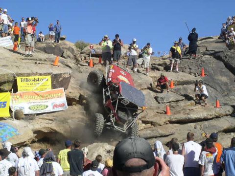 1979 Ford Bronco - An off-road buggy navigates a challenging rocky terrain during a competition, cheered on by a crowd of onlookers.