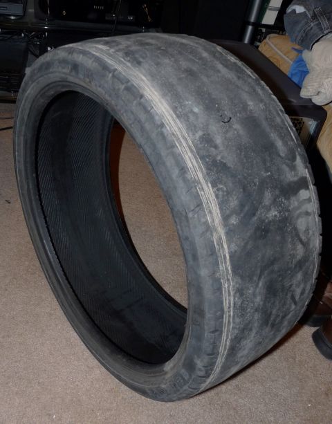 2006 Ford E350 - A worn low-profile performance tire standing on carpet indoors, its tread completely bald and corded to a slick surface with only faint rem…