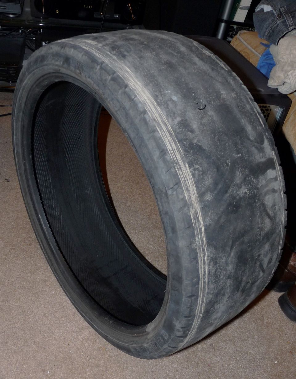 Bald worn-out low-profile performance tire standing on carpet indoors