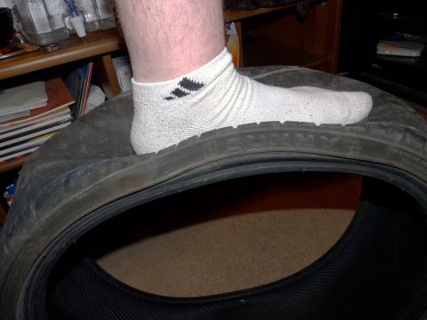 2006 Ford E350 - A dismounted low-profile Sunny tire lies on its side indoors, with a person's white-socked foot resting on the sidewall to show scale again…
