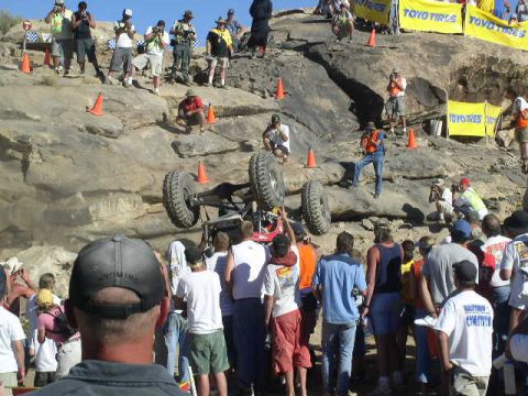 1979 Ford Bronco - An off-road vehicle is seen on its side during an event, with spectators gathered on a rocky incline.