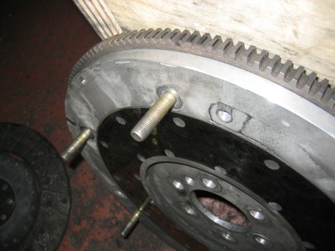 1998 Ford Crown Victoria - flywheel with a starter ring gear and an installed threaded alignment stud rests on a shop floor beside a worn clutch friction disc.