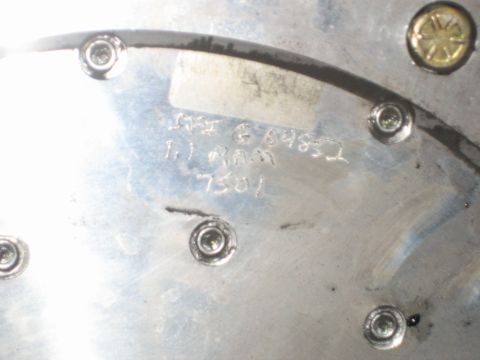 1998 Ford Crown Victoria - Close-up of the polished back face of a flywheel or pressure plate showing bolt holes, a paper label, and faint handwritten markings.
