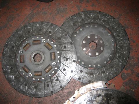 1998 Ford Crown Victoria - Two clutch friction discs with splined center hubs and sprung damper centers lie on a shop floor next to a metal part.