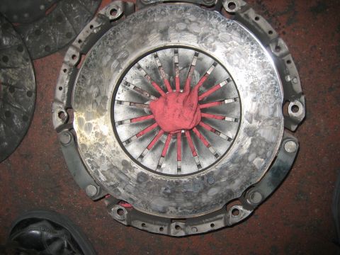 1998 Ford Crown Victoria - clutch pressure plate viewed from the diaphragm side, its spring fingers coated with red paint, lying on a shop floor.
