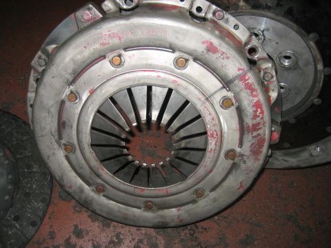 1998 Ford Crown Victoria - clutch pressure plate cover with a diaphragm spring and traces of red paint sits assembled with a flywheel on a shop floor.