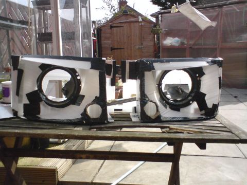 1989 Ford Bronco - Modified headlight housings, likely for a custom build, are displayed outdoors on a wooden table.