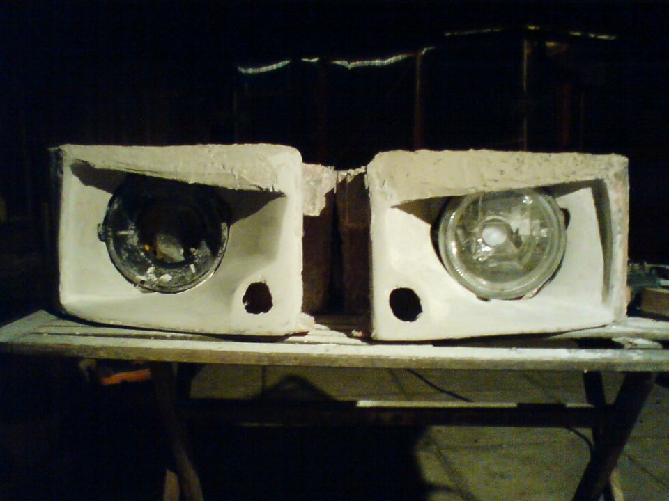 Two custom headlight housings with round headlights installed, sitting on a workbench