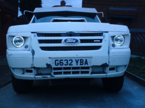 1989 Ford Bronco - Front view of a white van with a Ford emblem and custom halo headlights, showing signs of wear on the bumper.