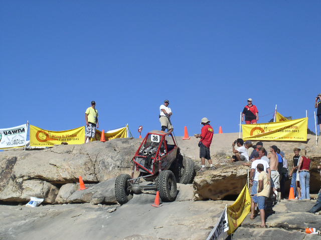 Red off-road buggy with number 36 on it navigating a rocky course with spectators watching