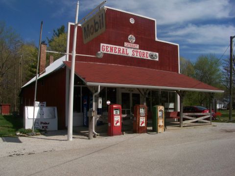 1989 Ford Bronco - A rural general store stands with vintage gas pumps out front and a red car parked under its covered porch.