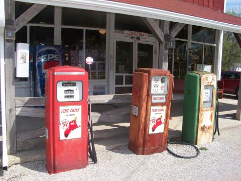 1989 Ford Bronco - Three vintage gas pumps, including a red Fire Chief model, stand outside an old general store.