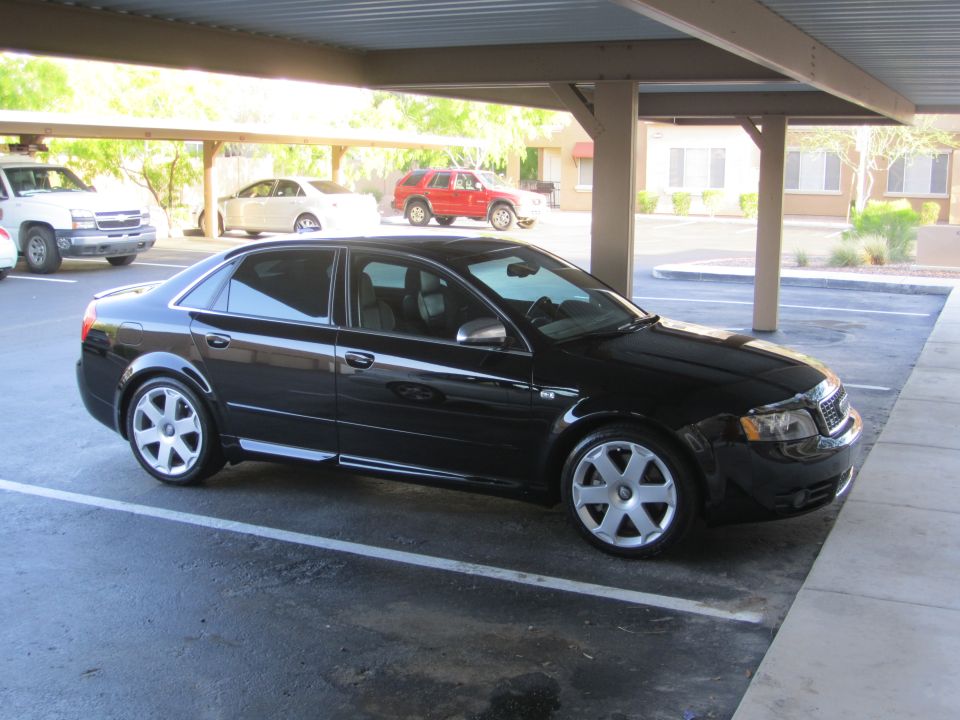 Black Audi sedan in profile under carport with silver seven-spoke wheels and chrome mirrors
