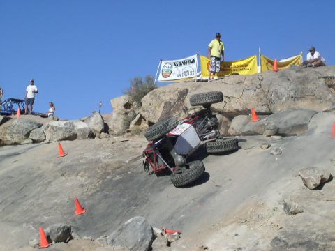 1979 Ford Bronco - An off-road vehicle has tipped onto its side during a competition on a rocky terrain, uneven terrain, with spectators watching from above.