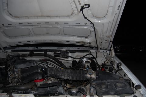 1994 Ford Bronco - Night-time flash photo into the engine bay of a white truck with the hood raised, showing the ribbed underside of the hood, the cowl and fi…