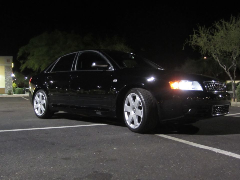 Black Audi S4 sedan at night in a parking lot, three-quarter front view with headlights on