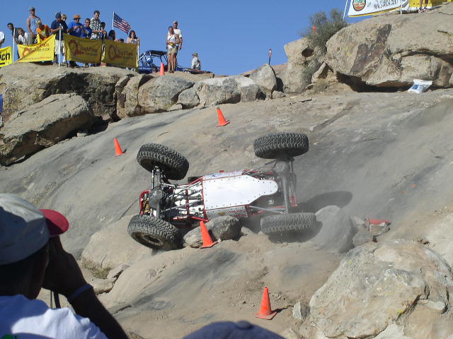 Off-road buggy overturned on a rocky hill during a competition. Spectators watch from above