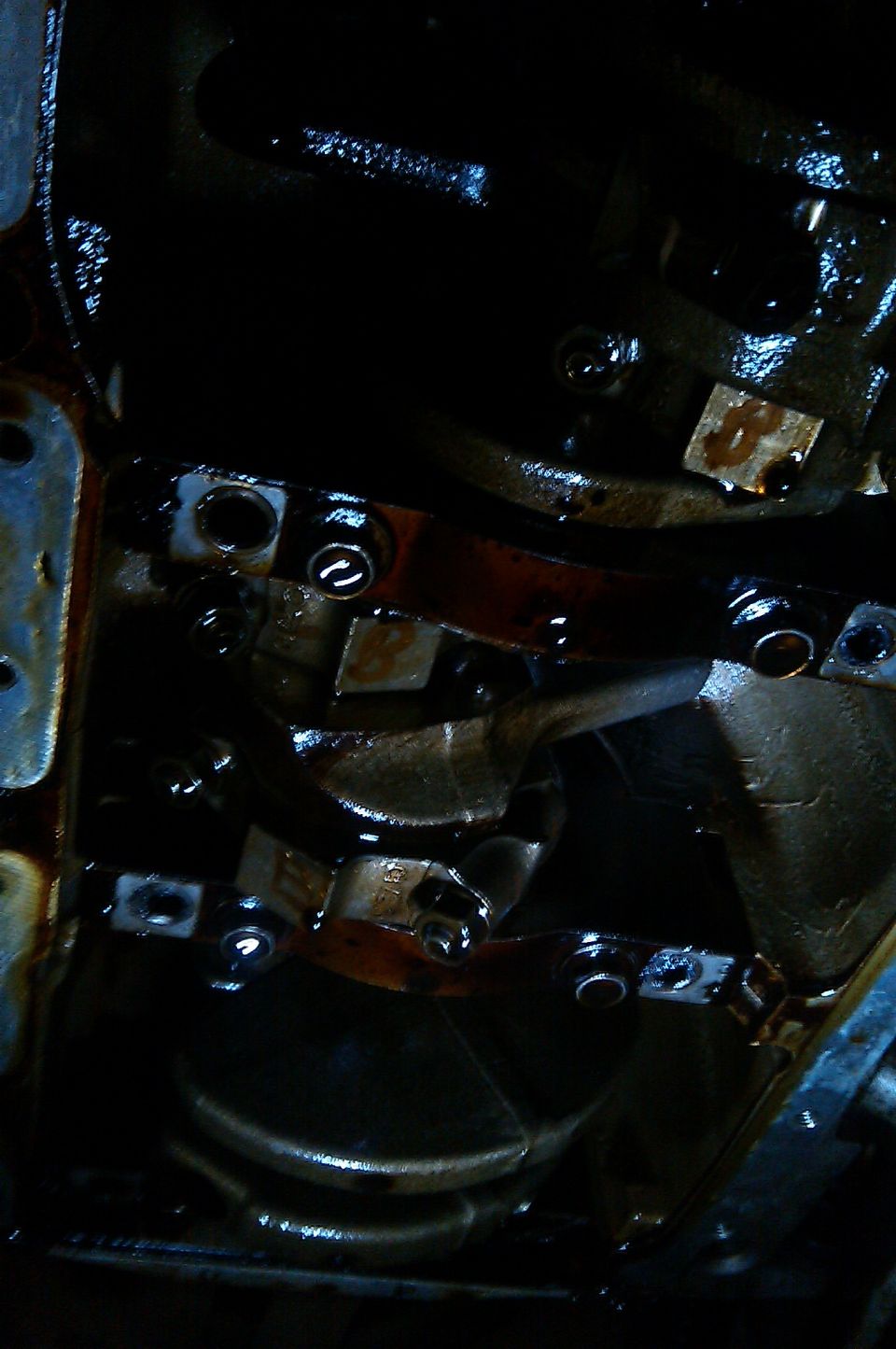 Engine crankshaft with connecting rod caps and bolts visible, covered in oil