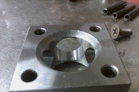 1999 Chevrolet Camaro - A machined metal component sits on a workbench next to a screw and several pins.