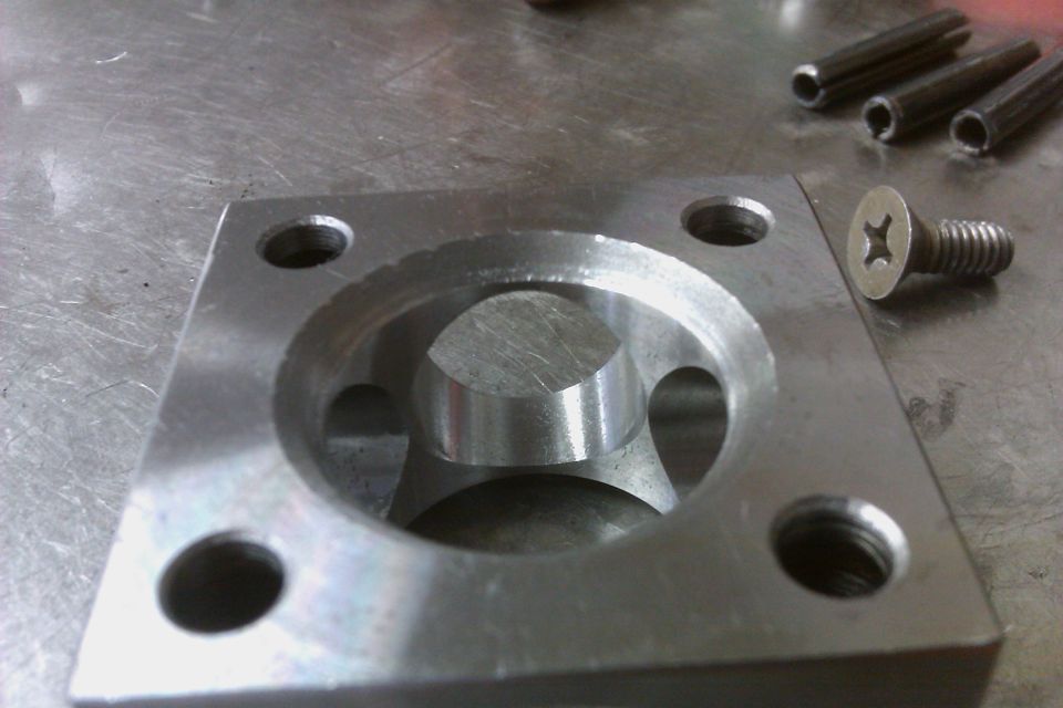 Close-up of a machined metal part with a screw and three pins nearby